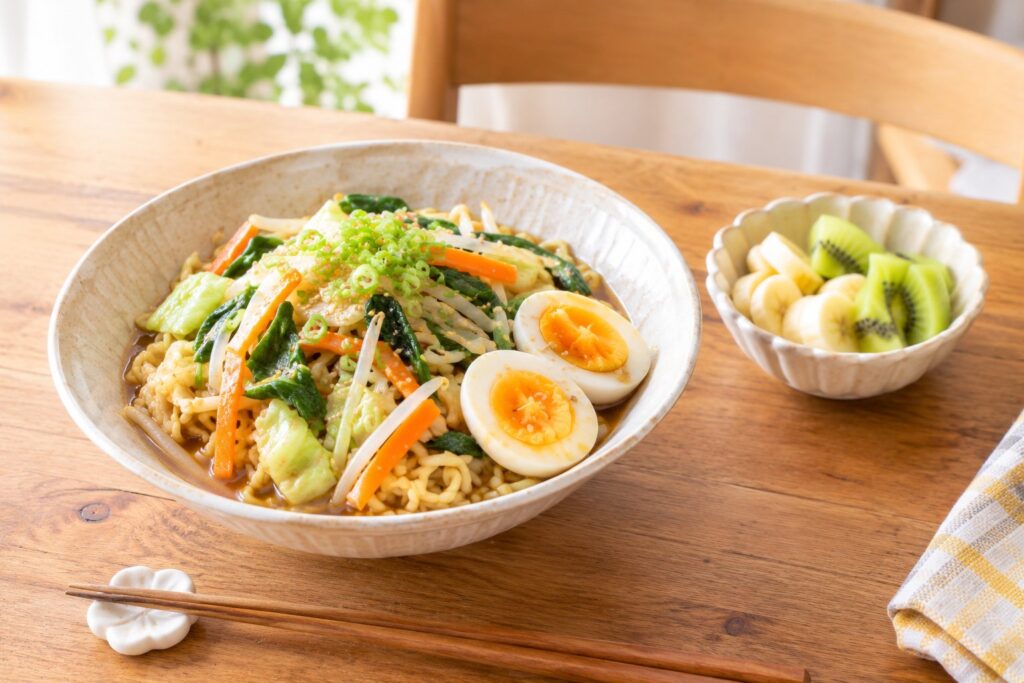 野菜とゆで卵をたっぷりのせたラーメンと、バナナとキウイの果物